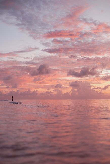 A lone figure stands in the ocean with a stunning sunset sky in the Cayman Islands.