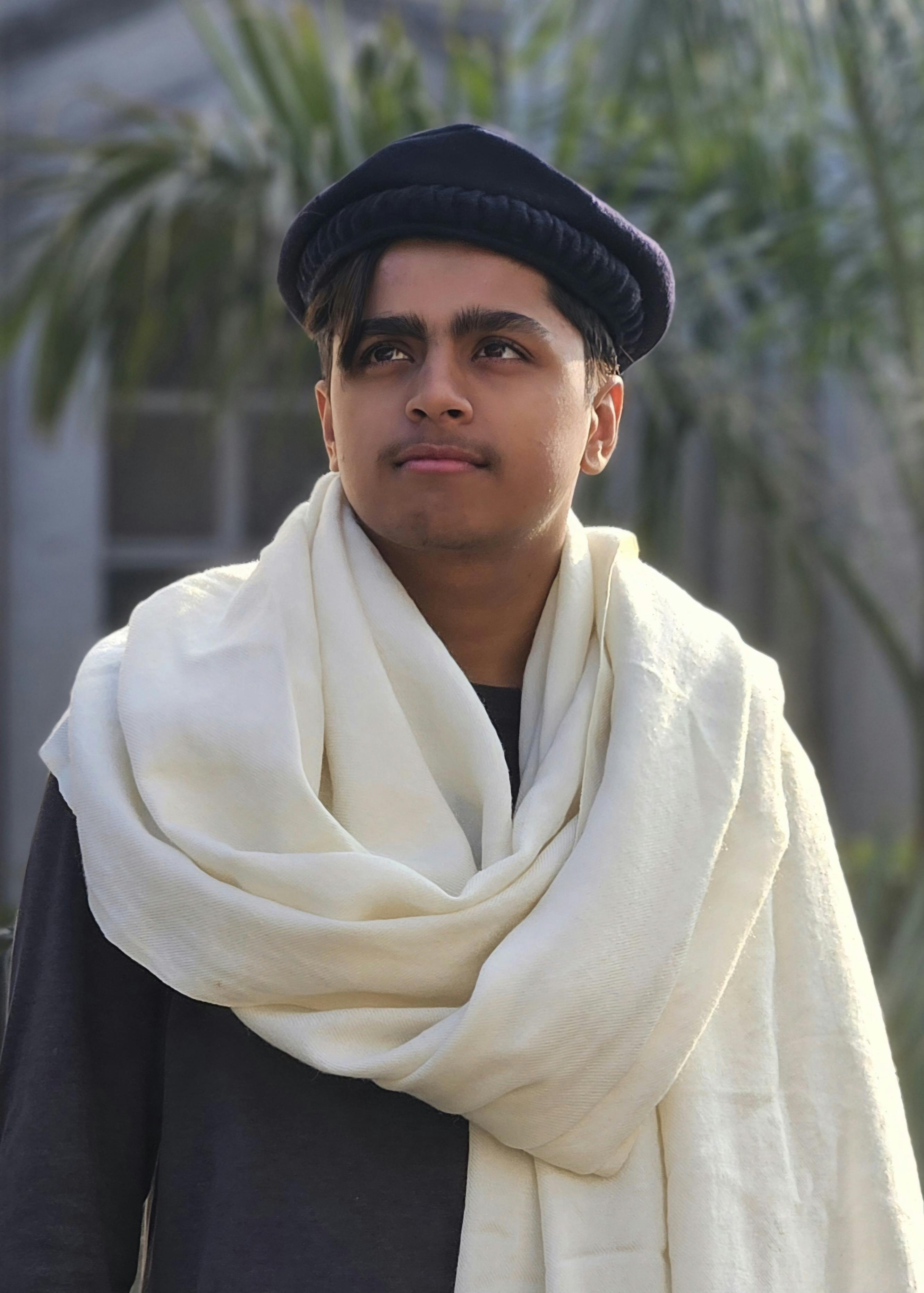 A young man in traditional clothing gazes thoughtfully outdoors, exuding cultural heritage.