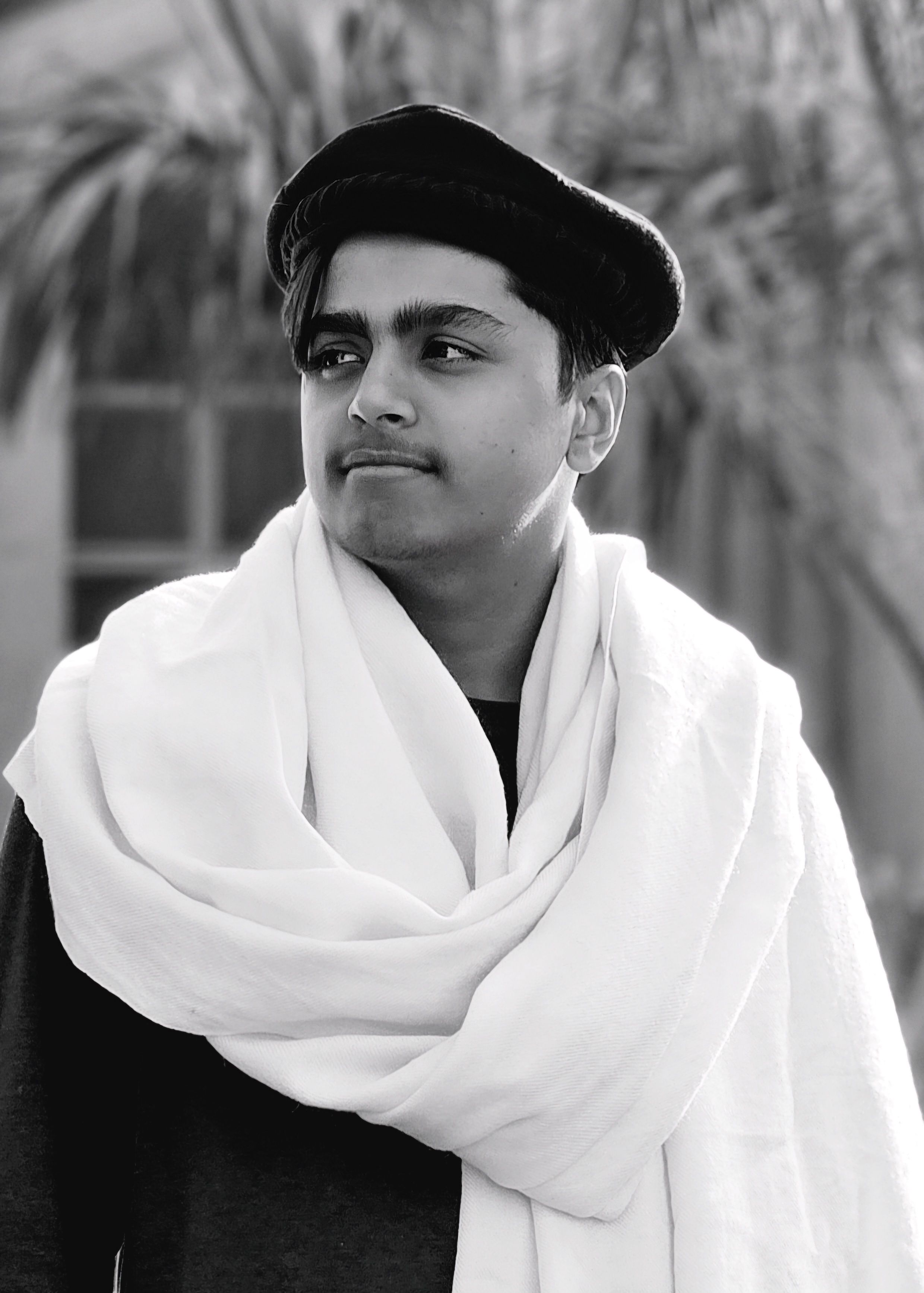 Black and white portrait of a young man wearing traditional attire with thoughtful expression outdoors.
