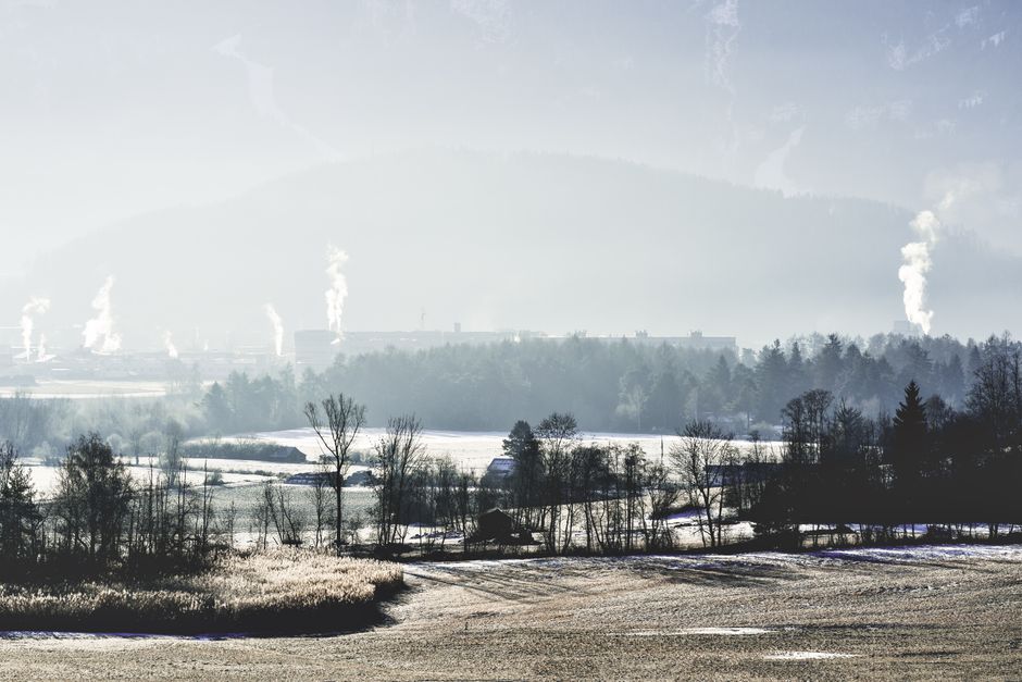 A tranquil winter scene featuring snow-covered fields and distant industrial factories emitting smoke.