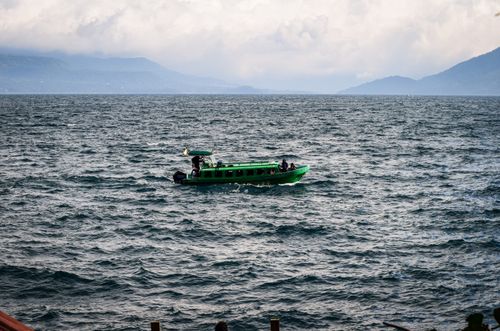 Free A vibrant green boat with passengers traverses a scenic lake surrounded by mountains. Stock Photo