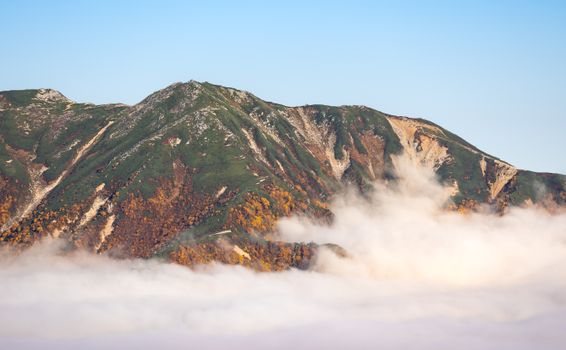 Captivating view of a mountain peak surrounded by autumn foliage and drifting clouds in the Japanese Alps.