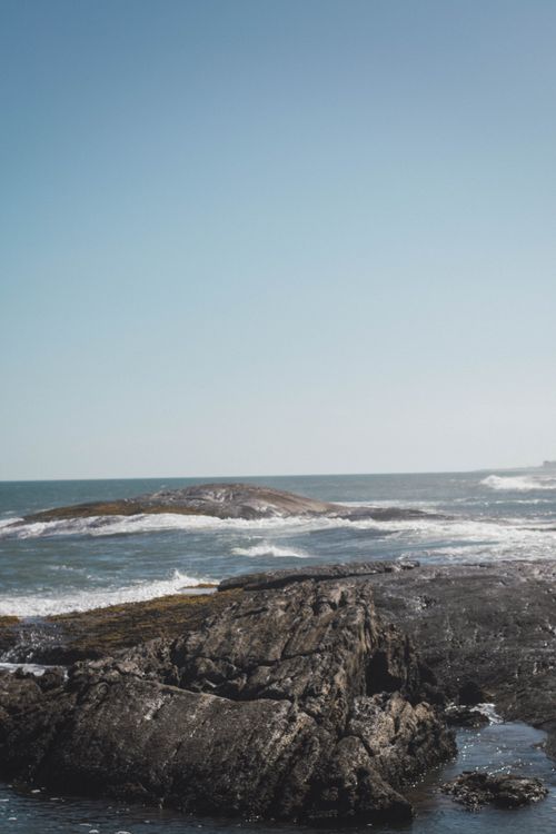 Free Serene ocean view of waves crashing on rugged rocks under a clear blue sky. Stock Photo
