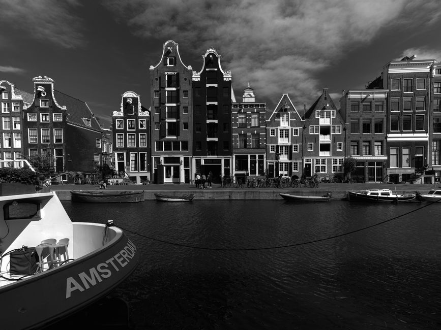 Black and white photo of iconic Amsterdam canal houses with boats.