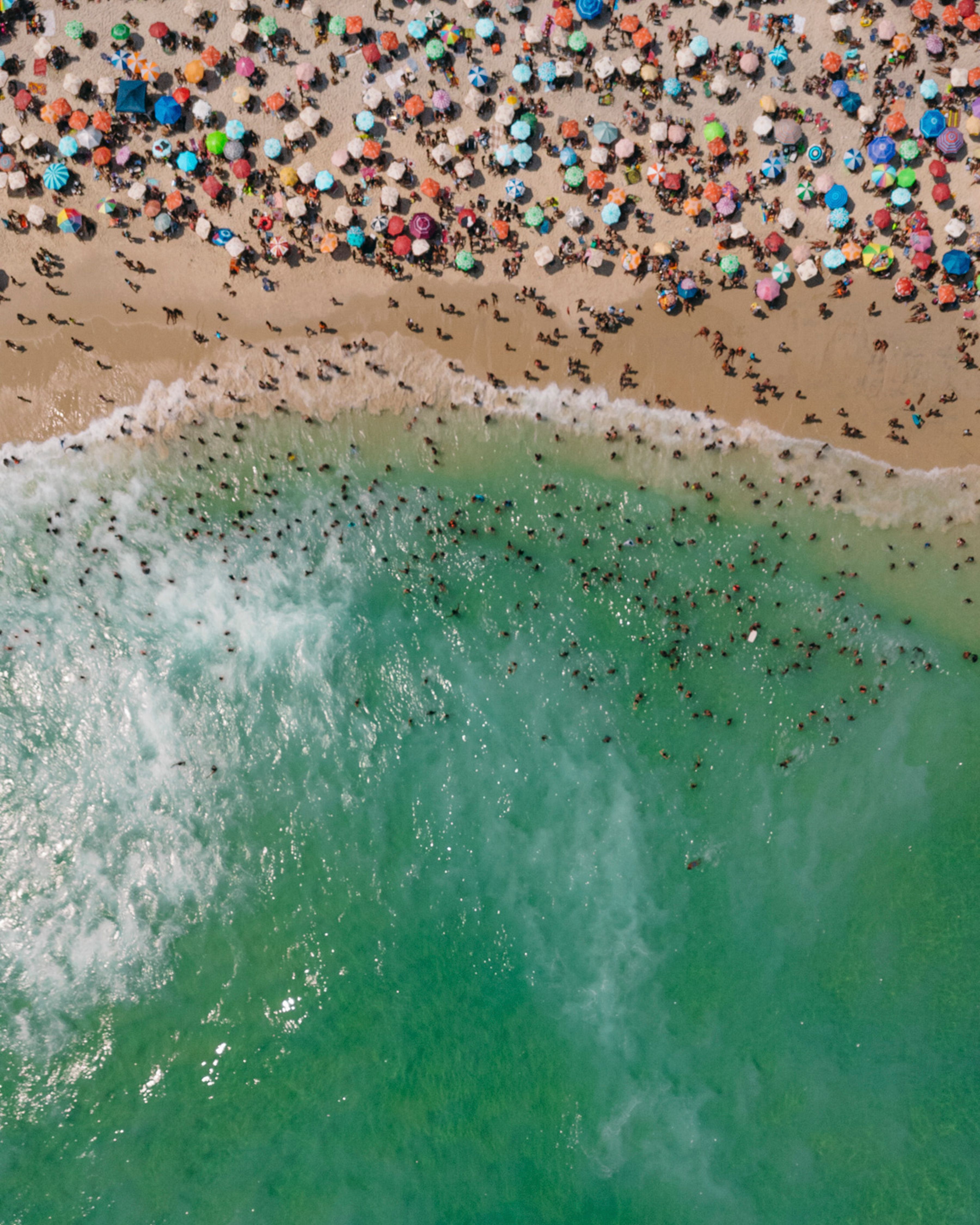 Vibrant aerial shot of Rio's crowded beach with colorful umbrellas and lively ocean waves.