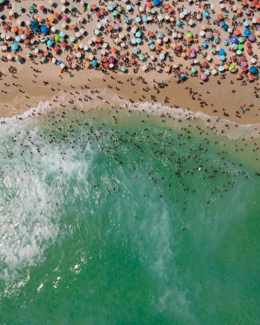 Vibrant aerial shot of Rio's crowded beach with colorful umbrellas and lively ocean waves.