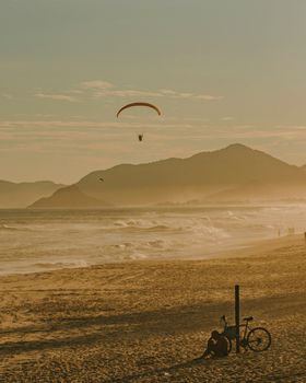 Experience the serene beauty of paragliding at sunset over a Rio de Janeiro beach with mountains in the distance.