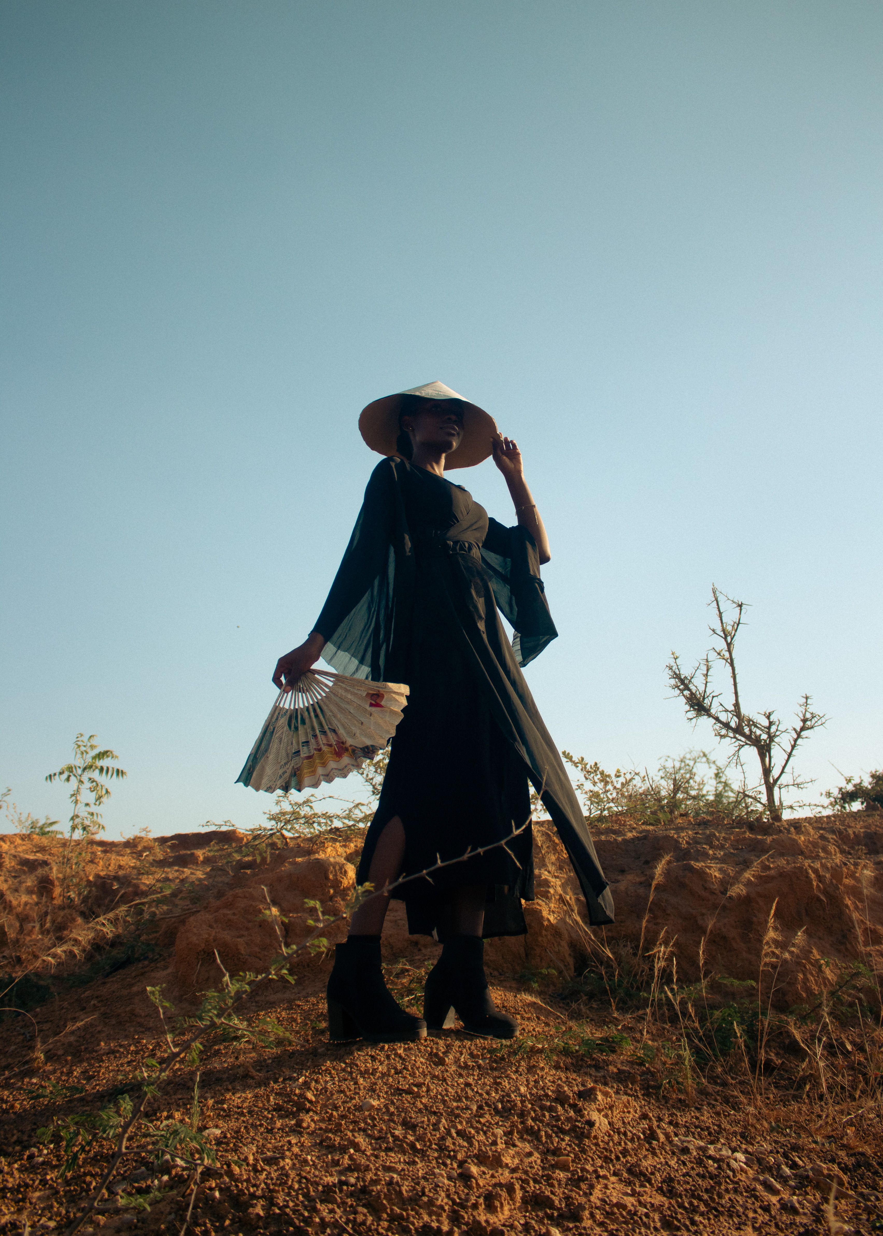 Stylish woman holds a fan in a desert setting, exuding elegance and mystery.