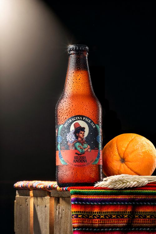 Free Chilled craft beer bottle with condensation, resting on a colorful Peruvian textile beside an orange. Stock Photo