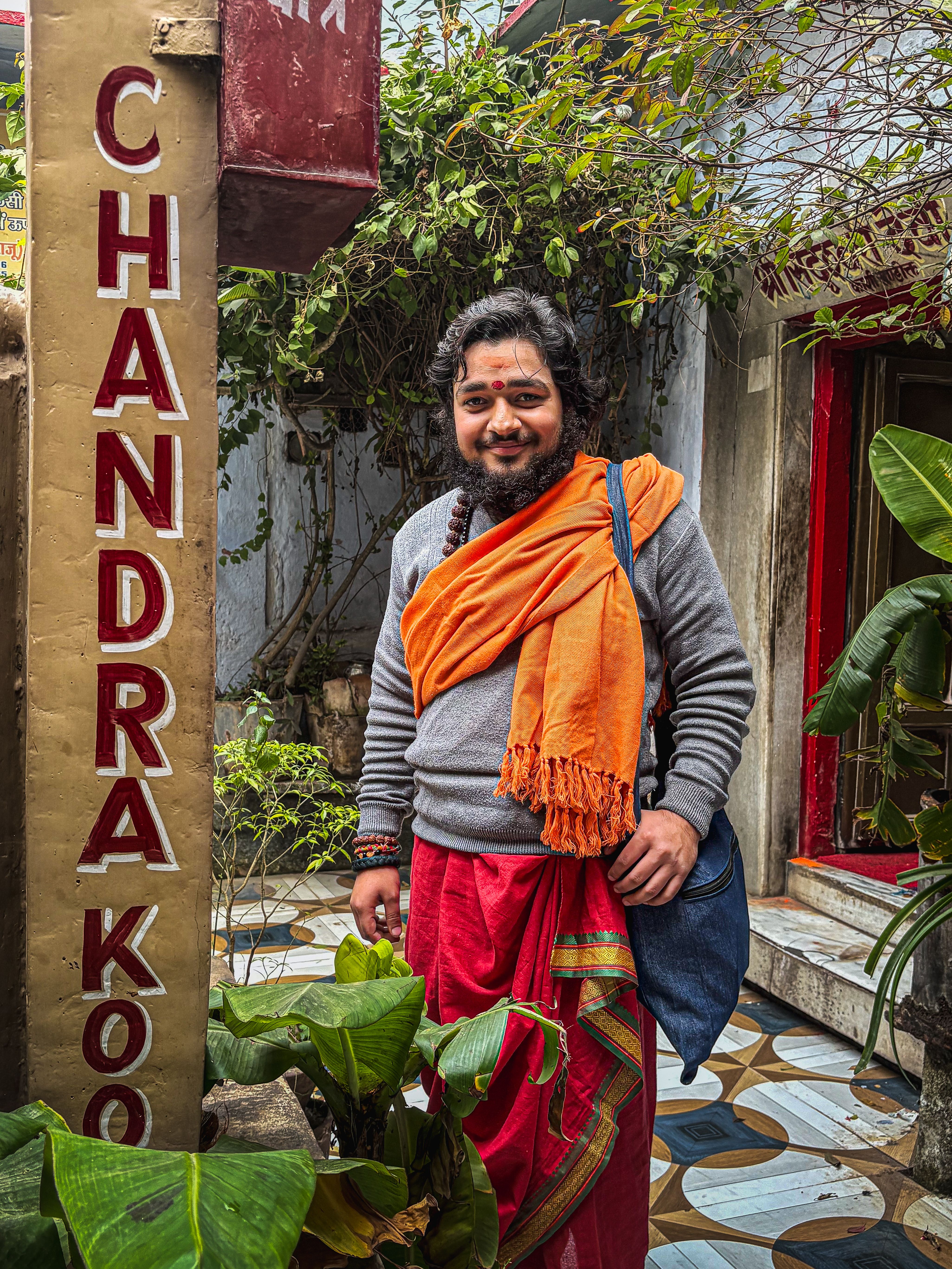 A cheerful man in vibrant traditional Indian clothing standing in a courtyard.