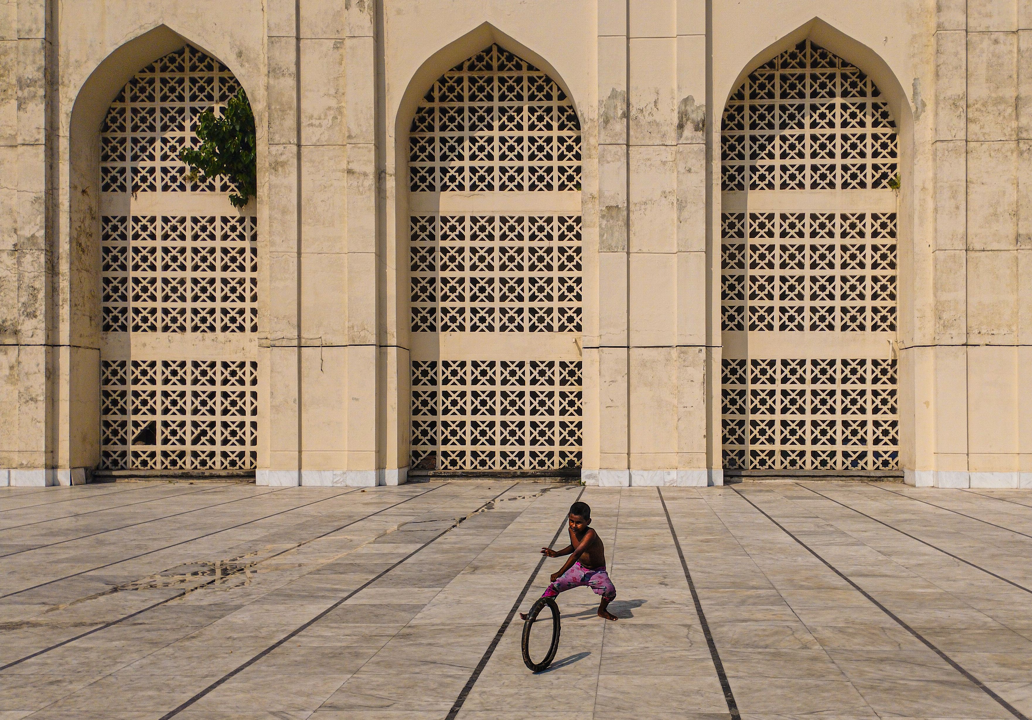 A child playfully rolls a hoop in front of an ornate architectural wall, capturing a moment of joy.