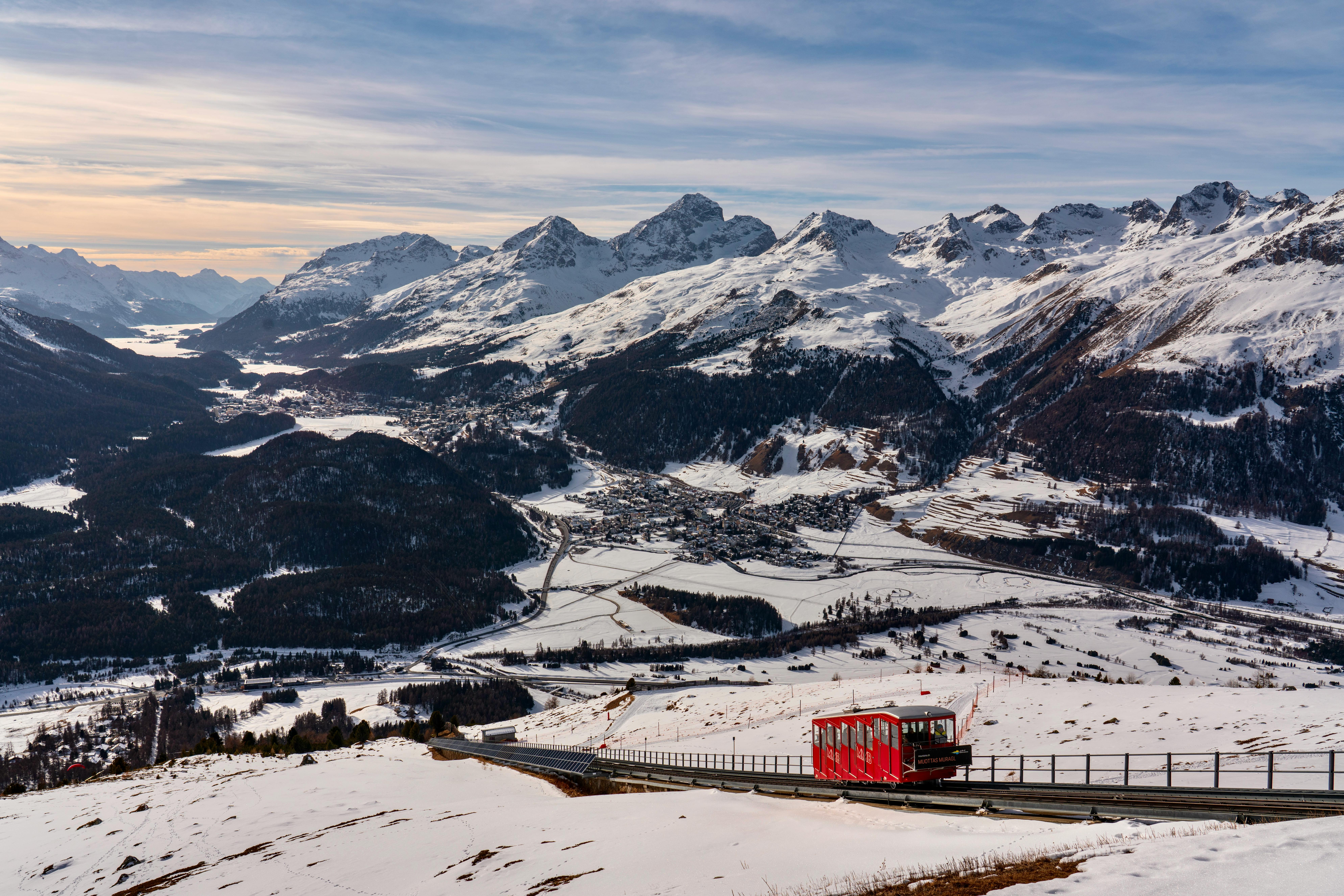 A vibrant red train traverses the snowy Swiss Alps, offering a breathtaking winter landscape view.