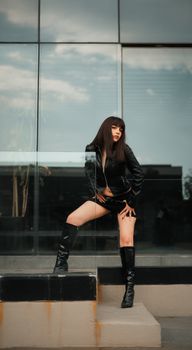 Woman posing confidently in a black leather outfit against modern architecture.