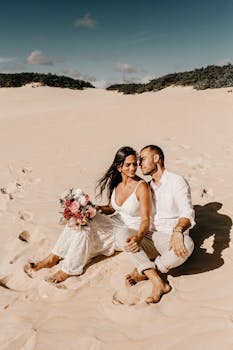 一对情侣幸福地坐在阳光明媚的海滩上，用花束分享浪漫时刻