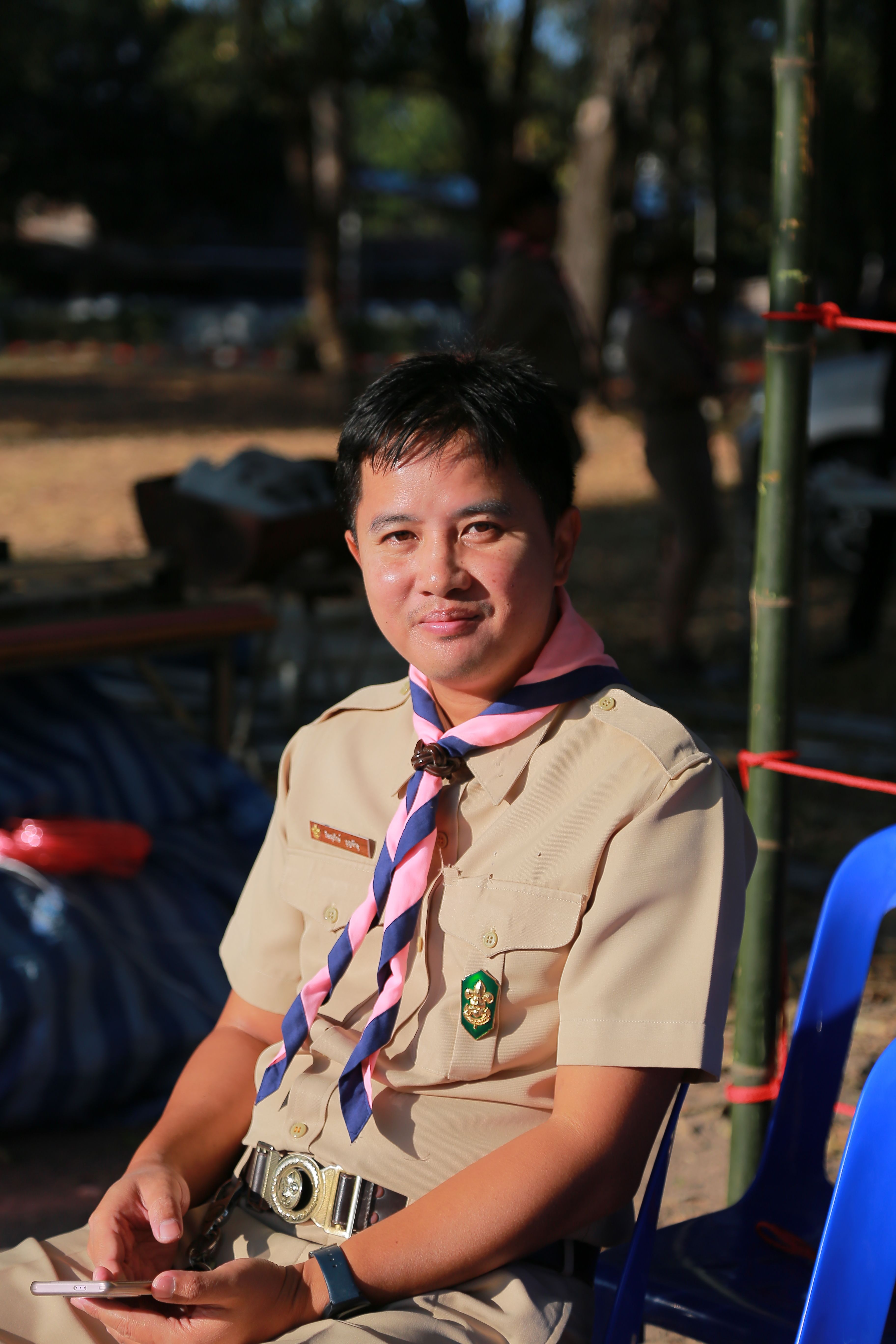 Scout leader in uniform sitting outdoors on a sunny day, smiling at the camera.