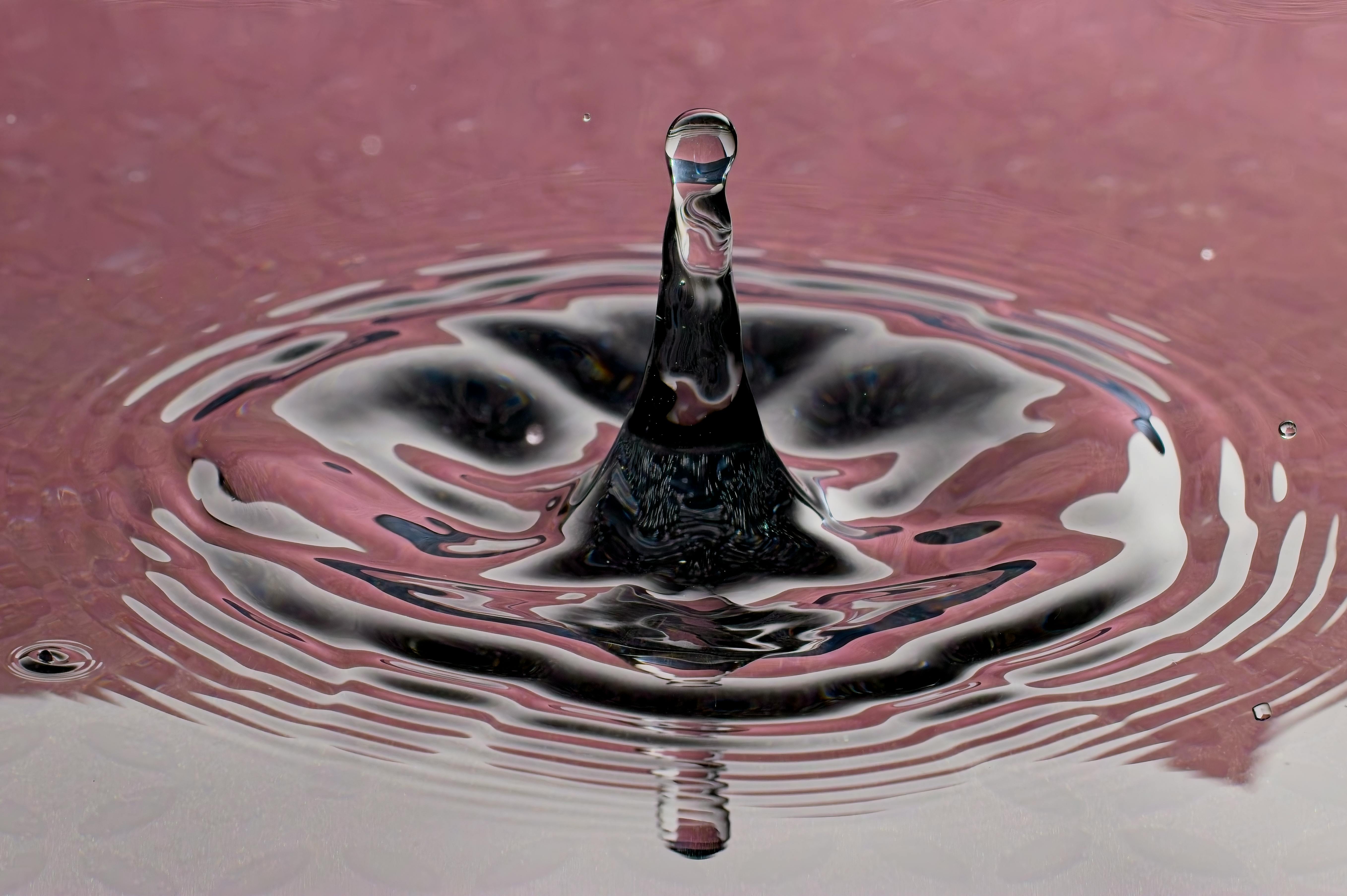 Captivating water droplet splash creating ripples on a pink surface, showcasing the beauty of fluid dynamics.