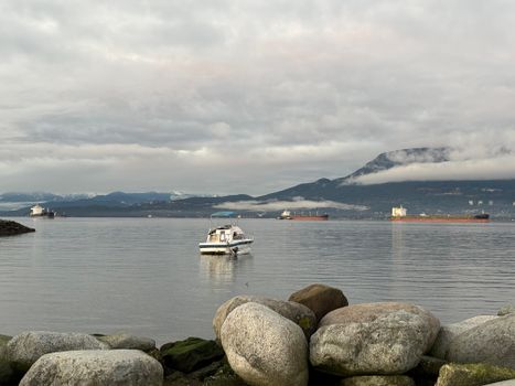 Calm morning view of Vancouver harbor with mountains and boats under a cloudy sky.