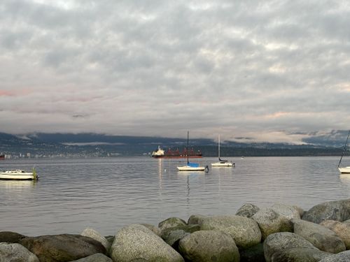 Free Peaceful scene of Vancouver harbour with sailboats and mountains under cloudy sky. Stock Photo