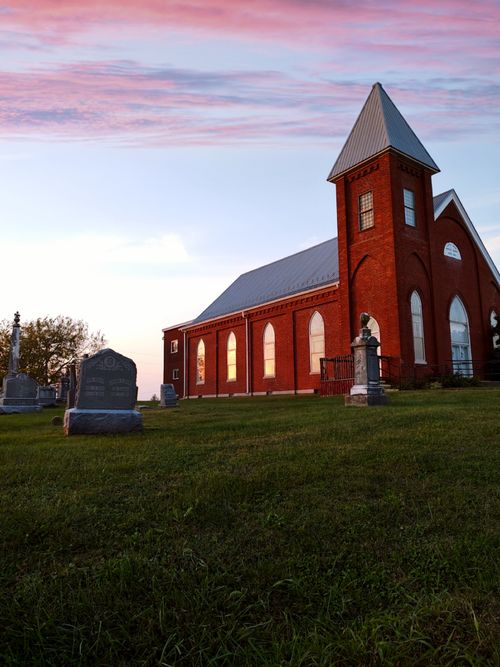 Free A serene red brick church beside a cemetery under a vibrant sunset sky. Stock Photo
