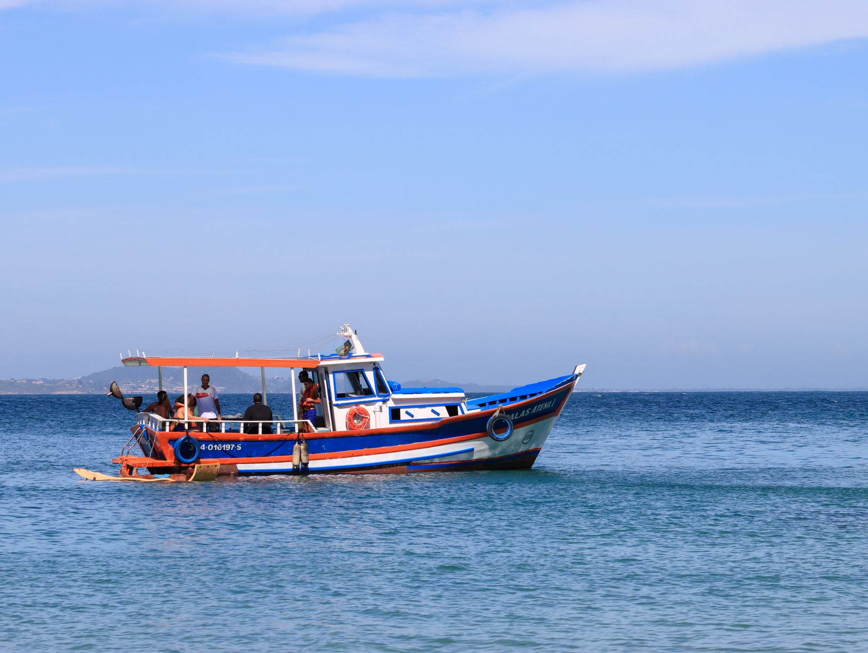 Vividly colored boat with passengers sailing in clear blue tropical waters under a bright sky.