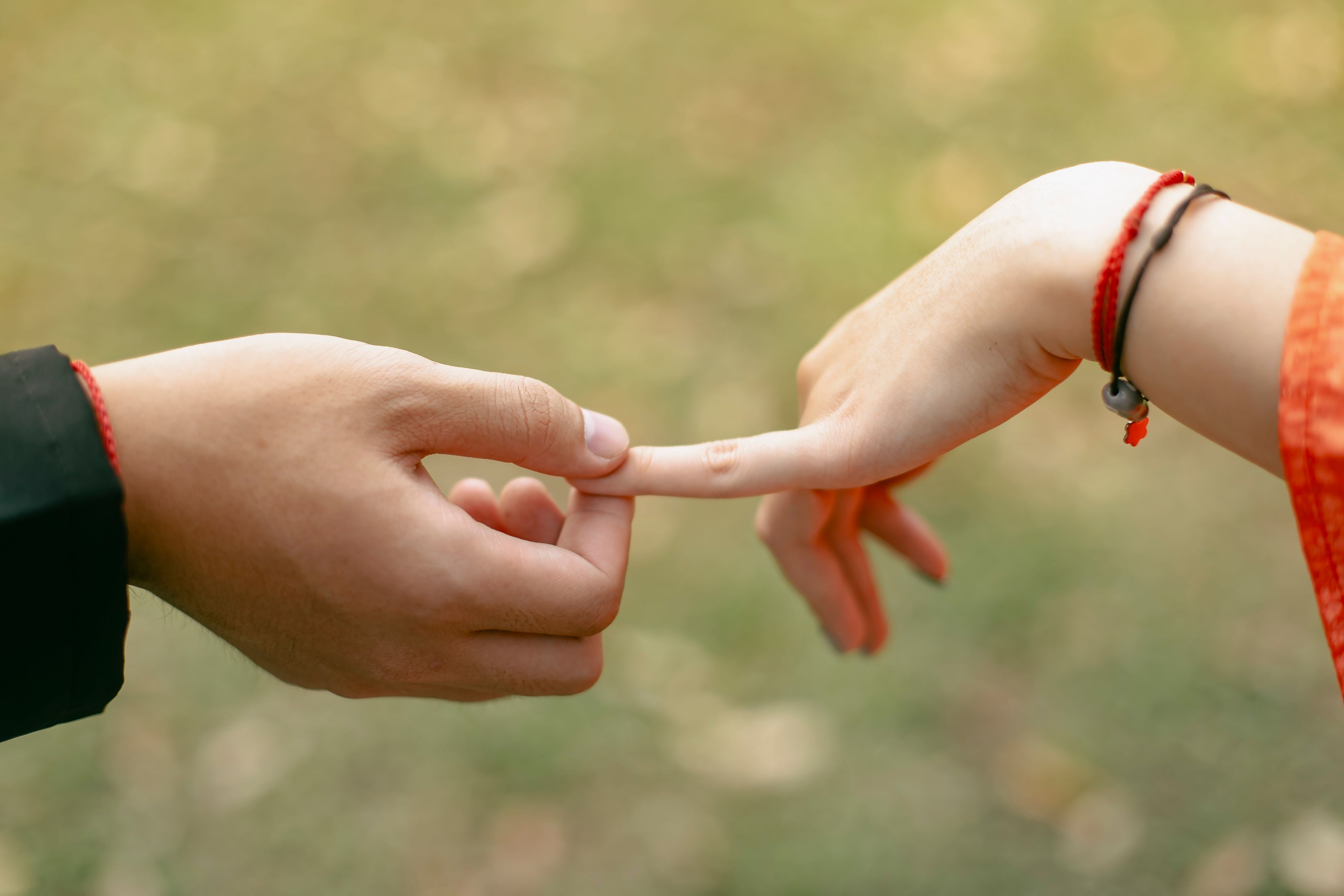 Close-up of two people's fingers gently touching, symbolizing connection and romance in an outdoor setting.