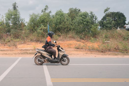 A person riding a scooter on a rural road with greenery in the background.