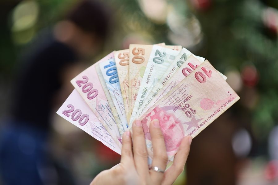 Close-up of a hand displaying various Turkish Lira banknotes outdoors.