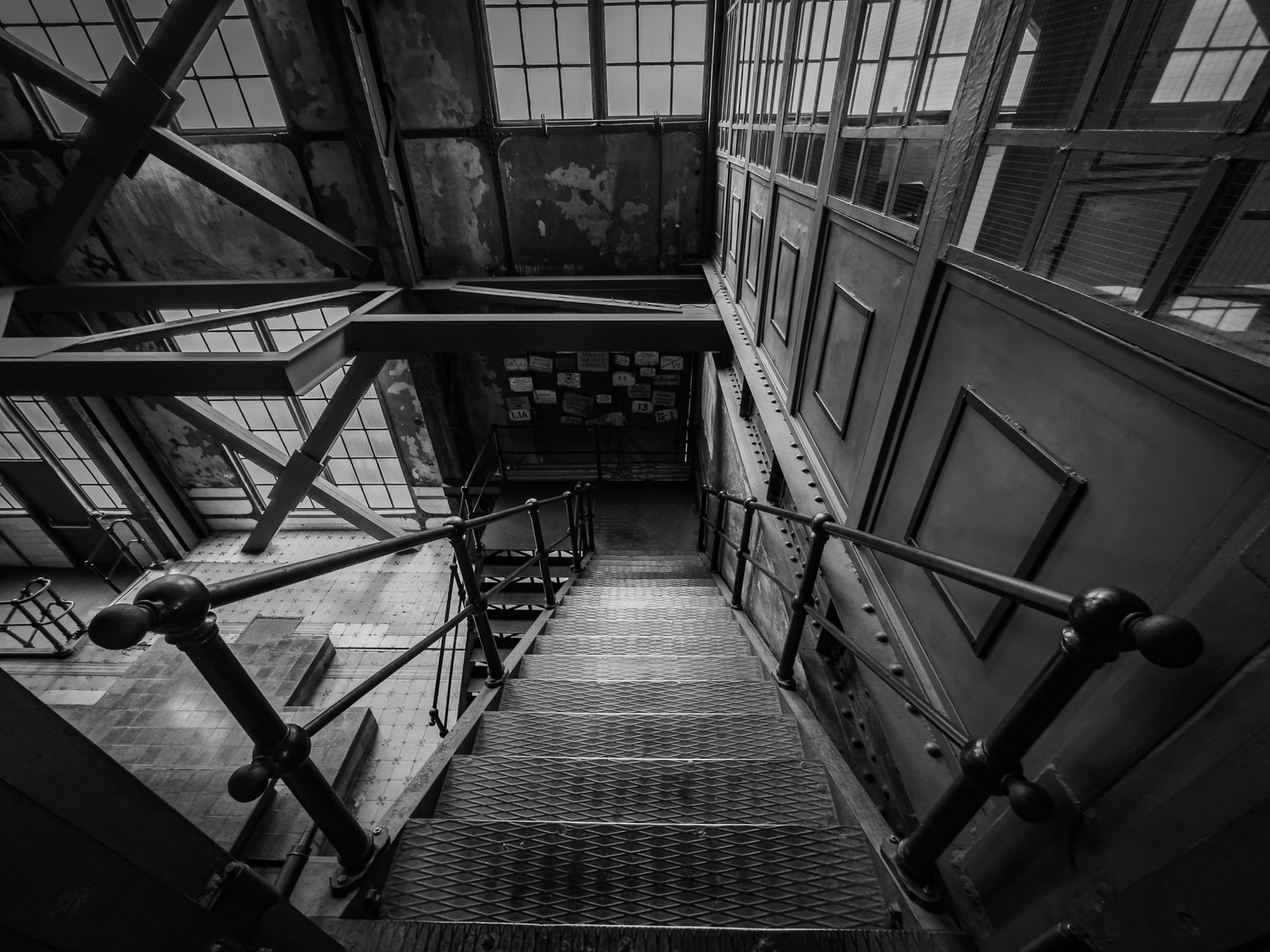 A black and white photograph of industrial stairs in an old building with steel beams.