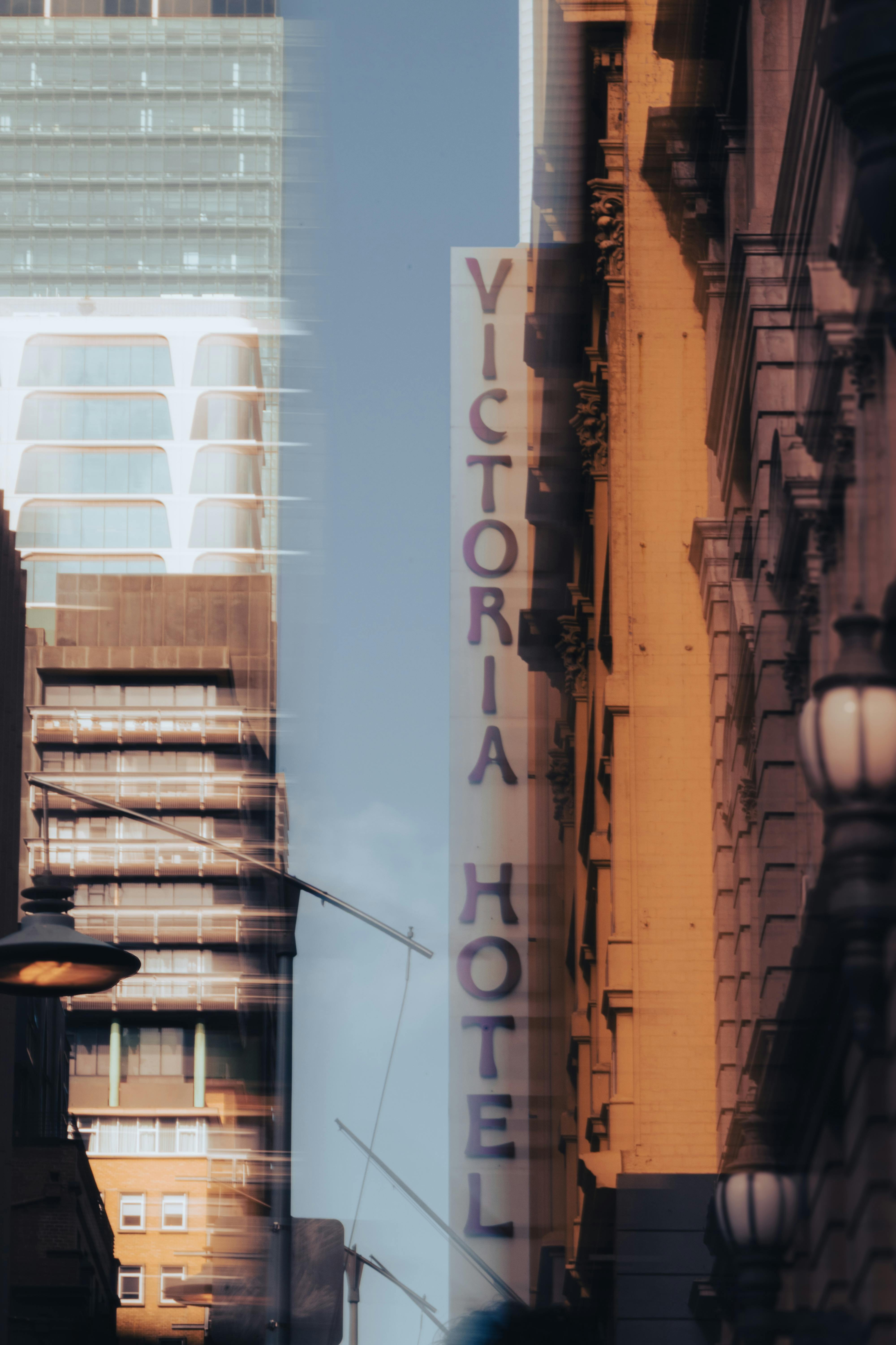 Gratis Pemandangan kota yang stylish menampilkan papan nama Victoria Hotel yang diapit oleh gedung-gedung tinggi. Foto Stok