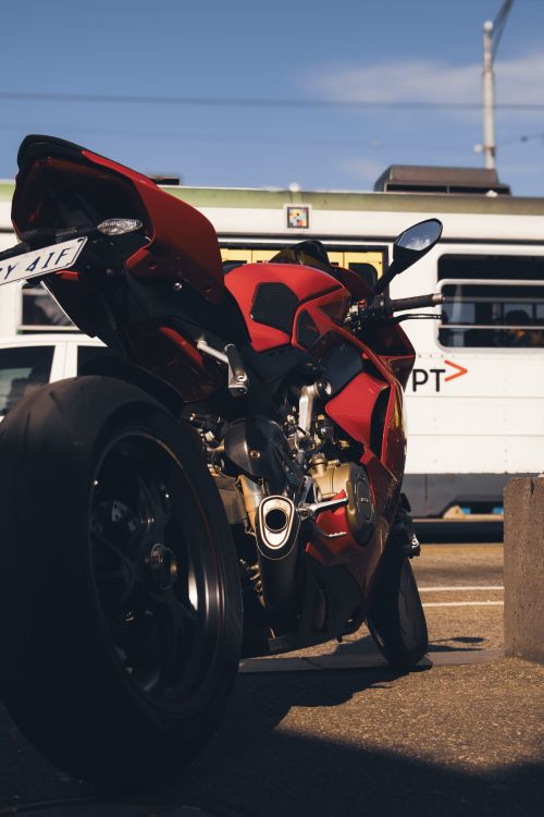 Free Vibrant red motorcycle parked on city street beside moving tram in daylight. Stock Photo