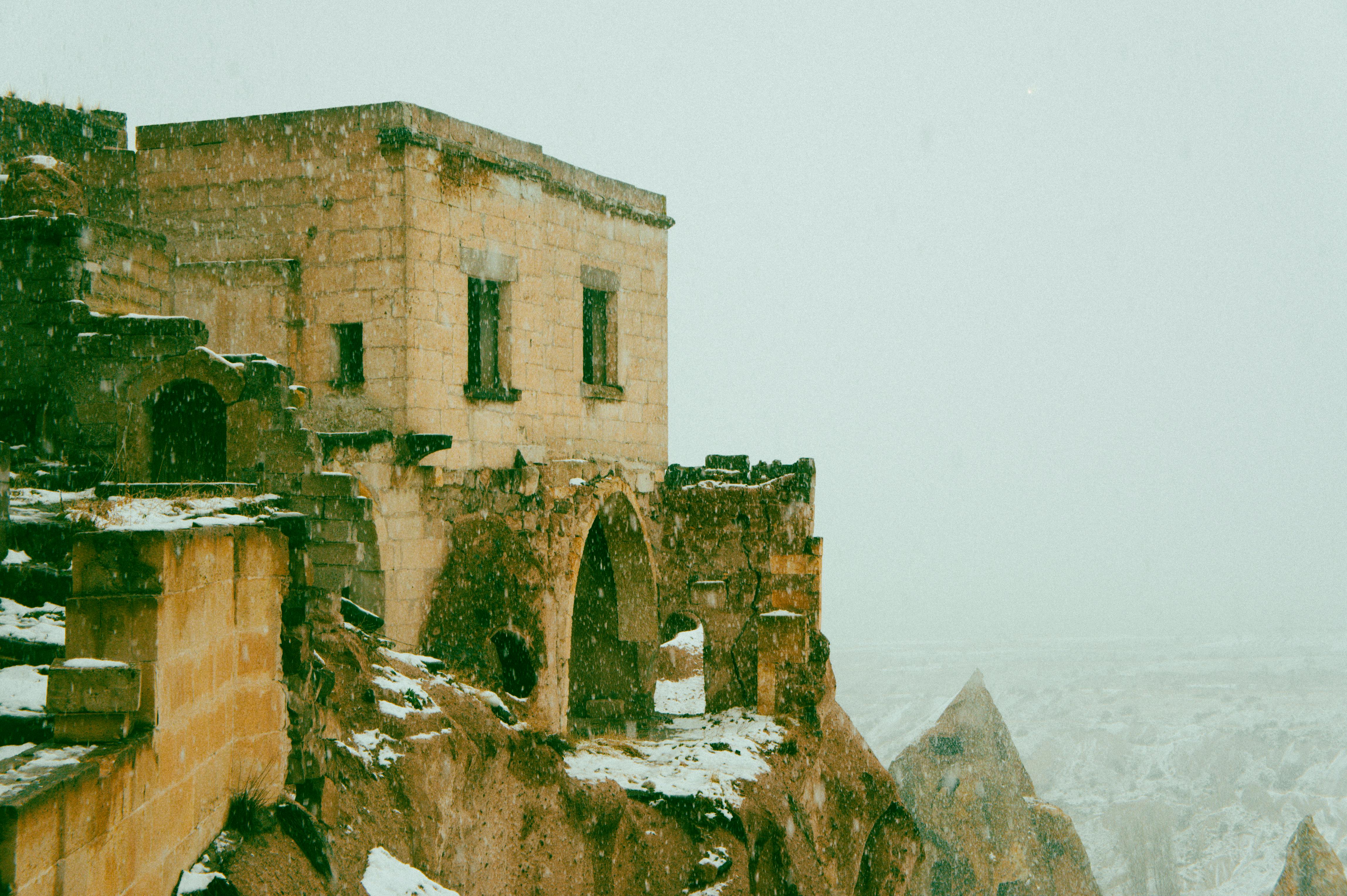 Old stone fortress in winter snow, showcasing historic architecture against a foggy backdrop.