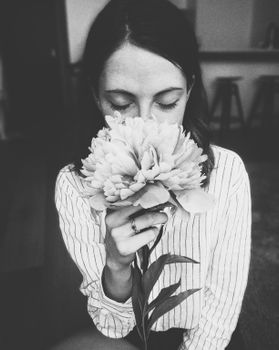 一幅黑白肖像画中，一位闭着眼睛的女人在室内闻到了牡丹花的味道