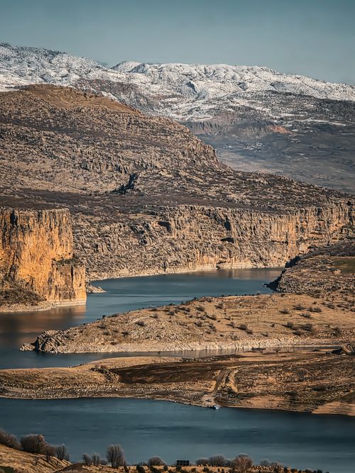 Free Beautiful view of Adıyaman with rocky cliffs, serene river, and distant snow-capped mountains. Stock Photo