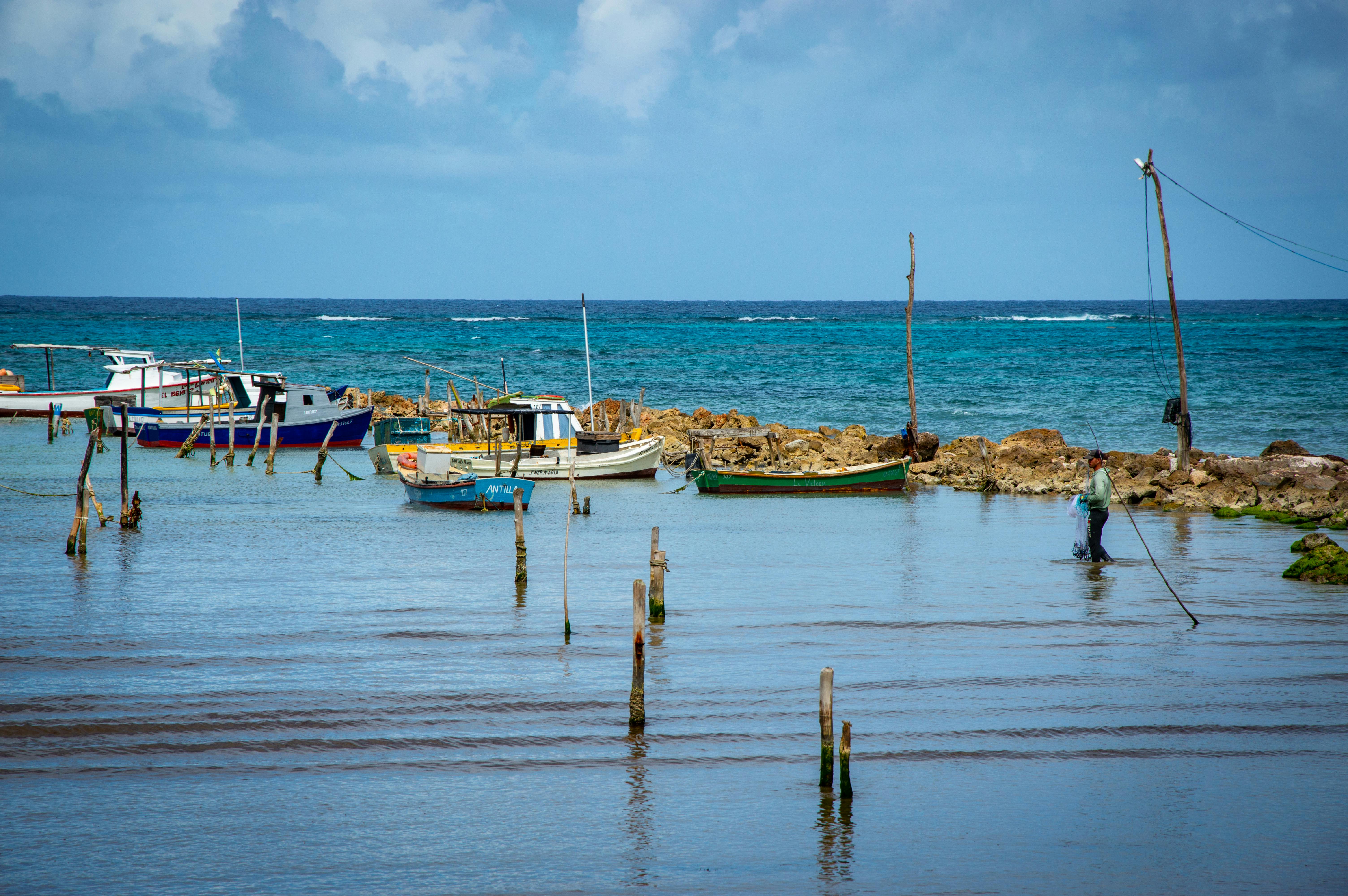 Tranquil seascape featuring fishing boats and fisherman by rocky coast.