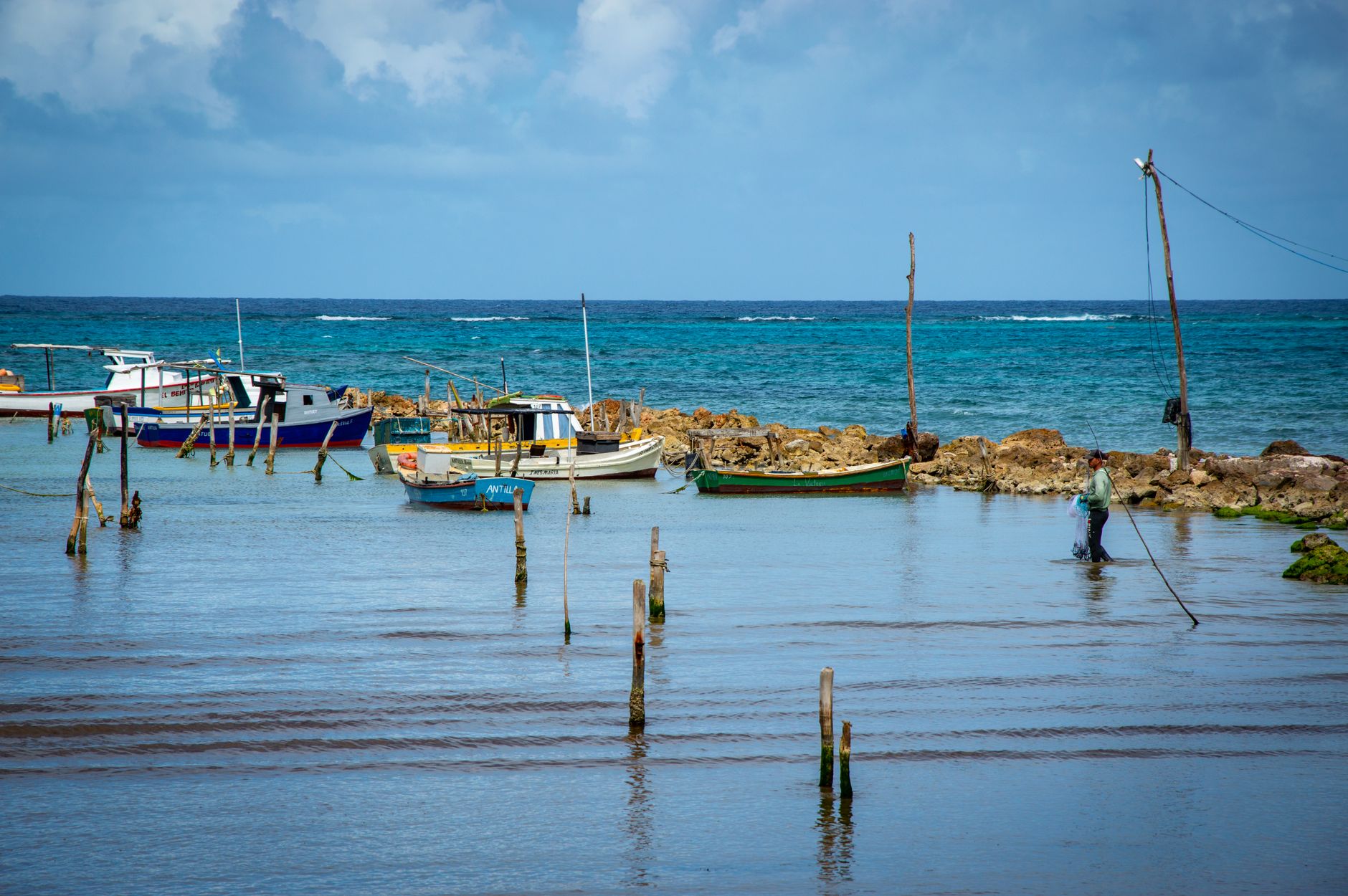 Tranquil seascape featuring fishing boats and fisherman by rocky coast.