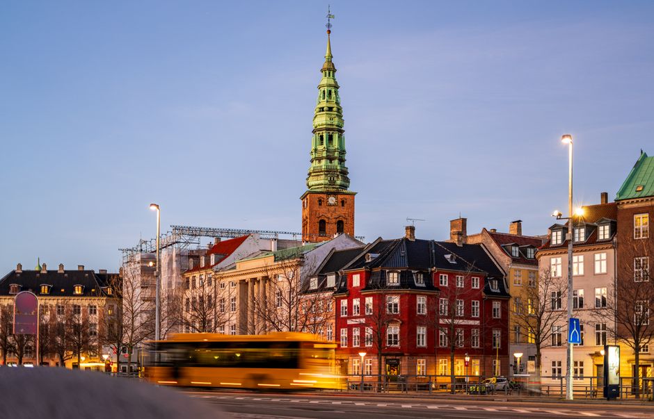 Copenhagen cityscape at dusk featuring historic buildings and a moving yellow bus.