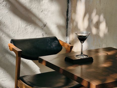 A martini glass casting shadows on a wooden table in a sunlit cafe in Haiphong, Vietnam.