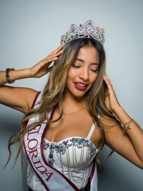 A young woman wearing a crown and sash smiles confidently.
