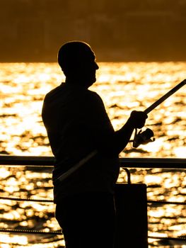 Silhouette of a man fishing at sunset with golden reflections on the water.