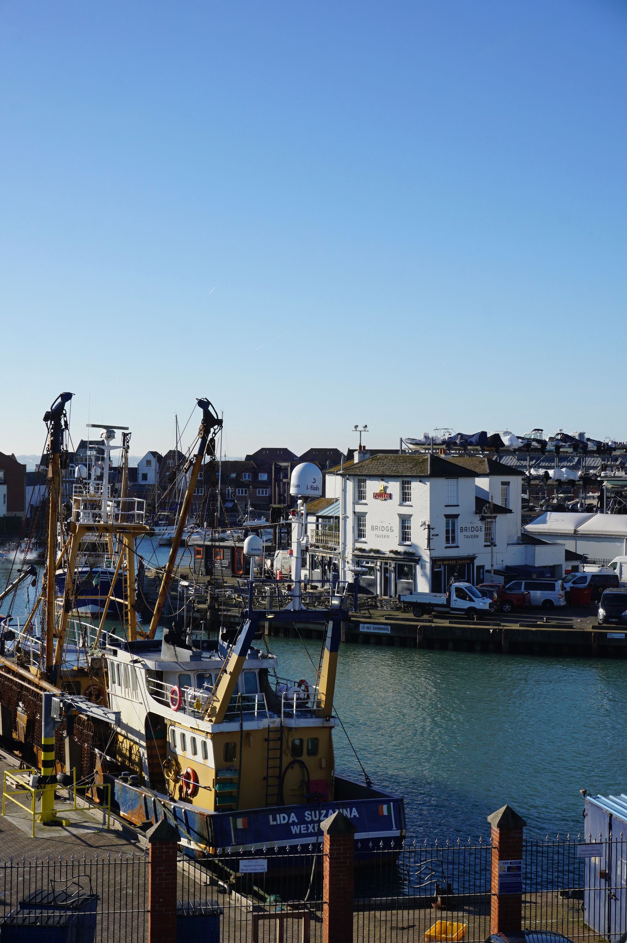 Scenic view of fishing boats docked at Portsmouth harbor in England under a clear sky.