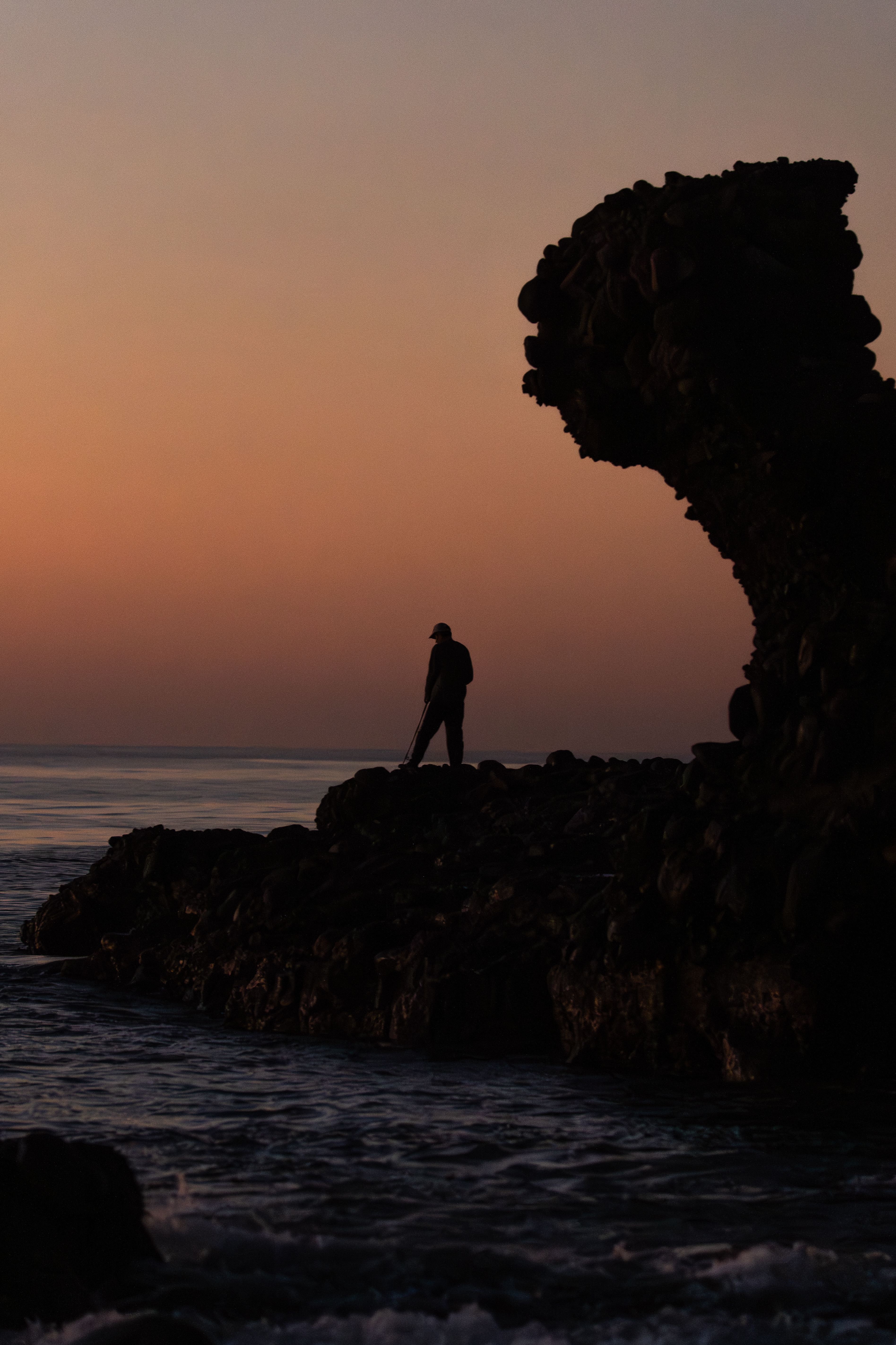 A silhouette of a person standing on a rocky shore at sunset, capturing a serene ocean view.