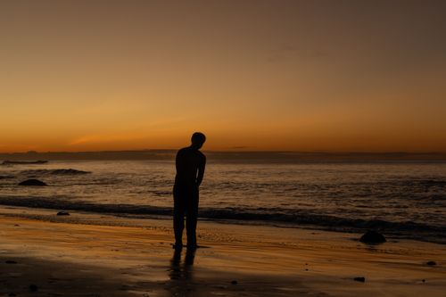 Free A silhouette of a person standing on a beach during a breathtaking sunset. Stock Photo