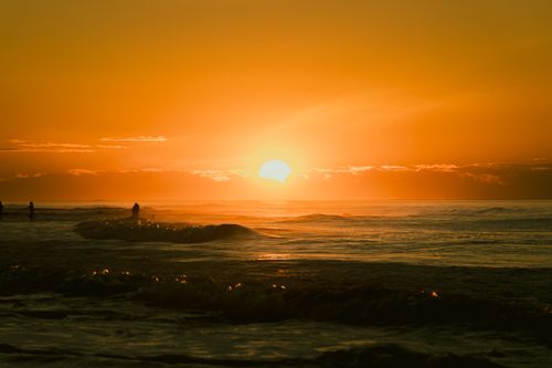 Free A tranquil sunset over the ocean with silhouetted surfers riding gentle waves. Stock Photo