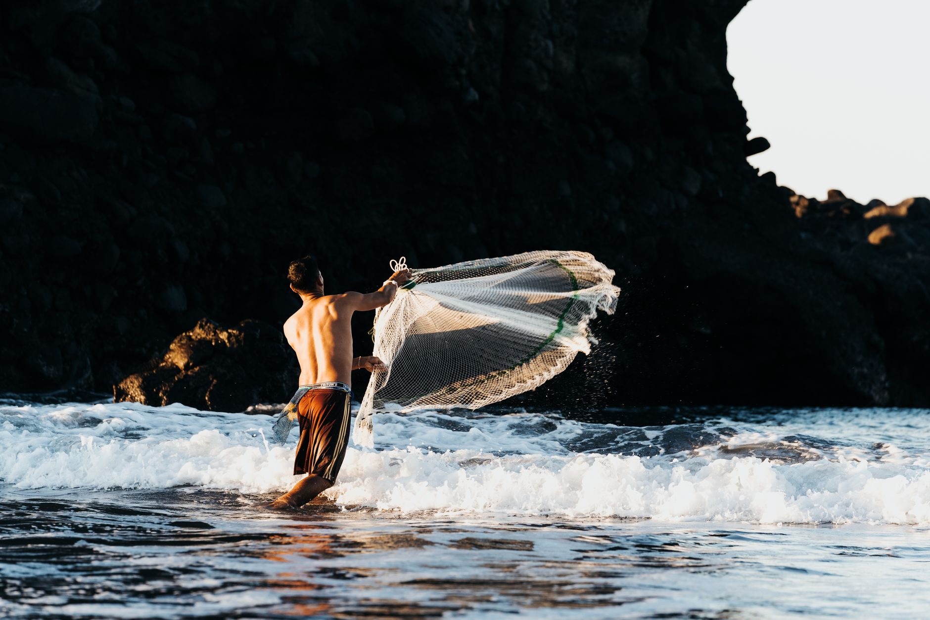 A fisherman casts his net into the ocean waves along the rocky shoreline of El Tunco, El Salvador.
