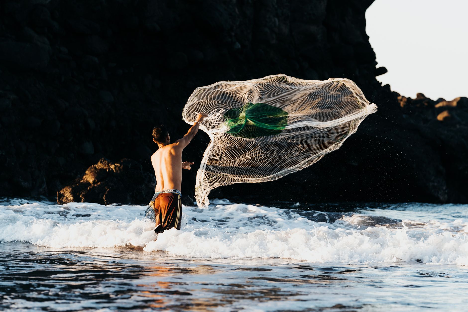 A fisherman skillfully casting a net in the waves of El Tunco Beach, El Salvador.