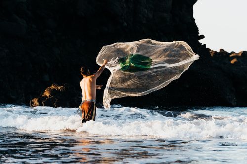Free A fisherman skillfully casting a net in the waves of El Tunco Beach, El Salvador. Stock Photo