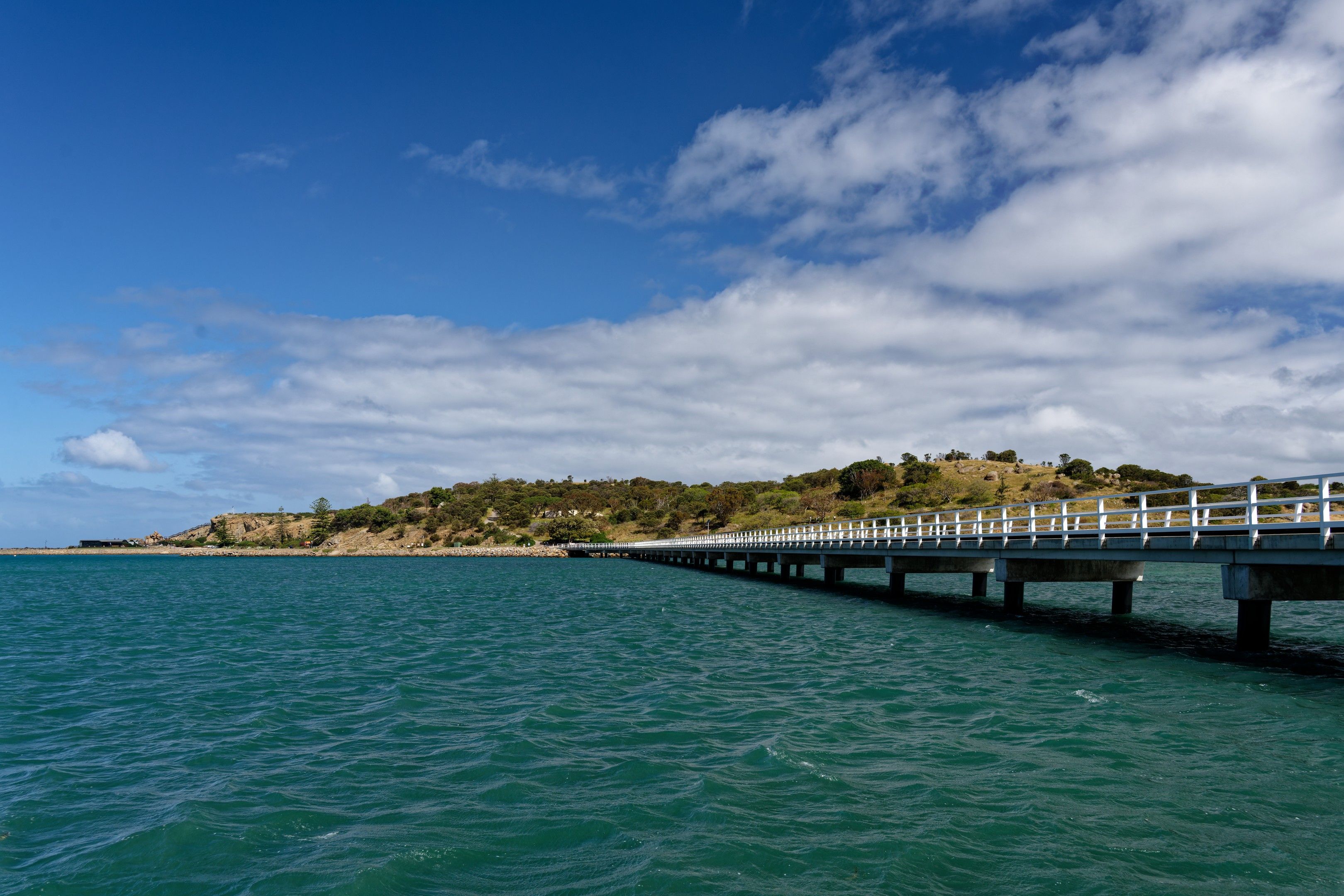 Long pier stretching into the sea with a scenic view of the coastline under a bright blue sky in Victor Harbor, Australia.