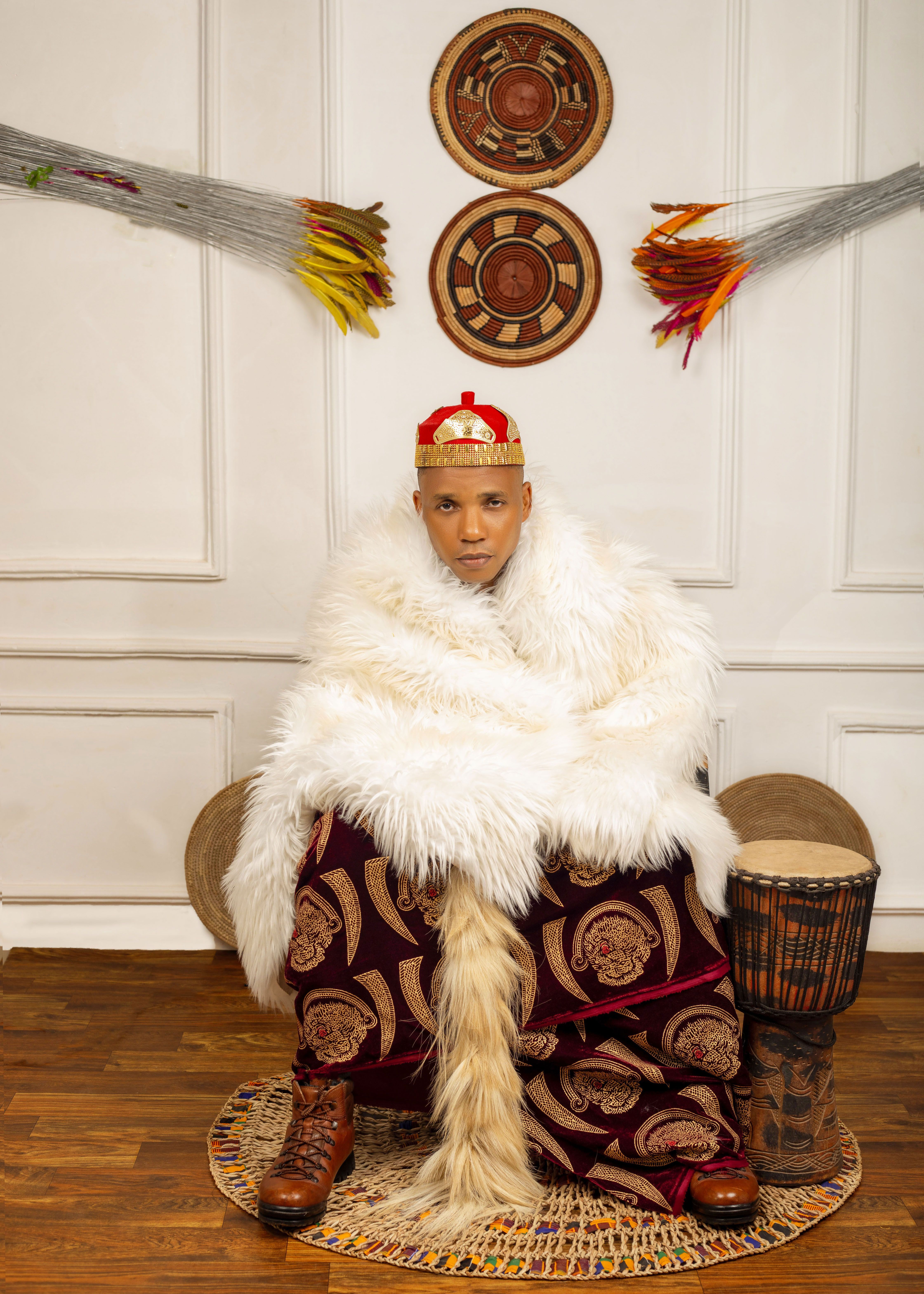Person in traditional attire with fur shawl and drum in an artistic setting.