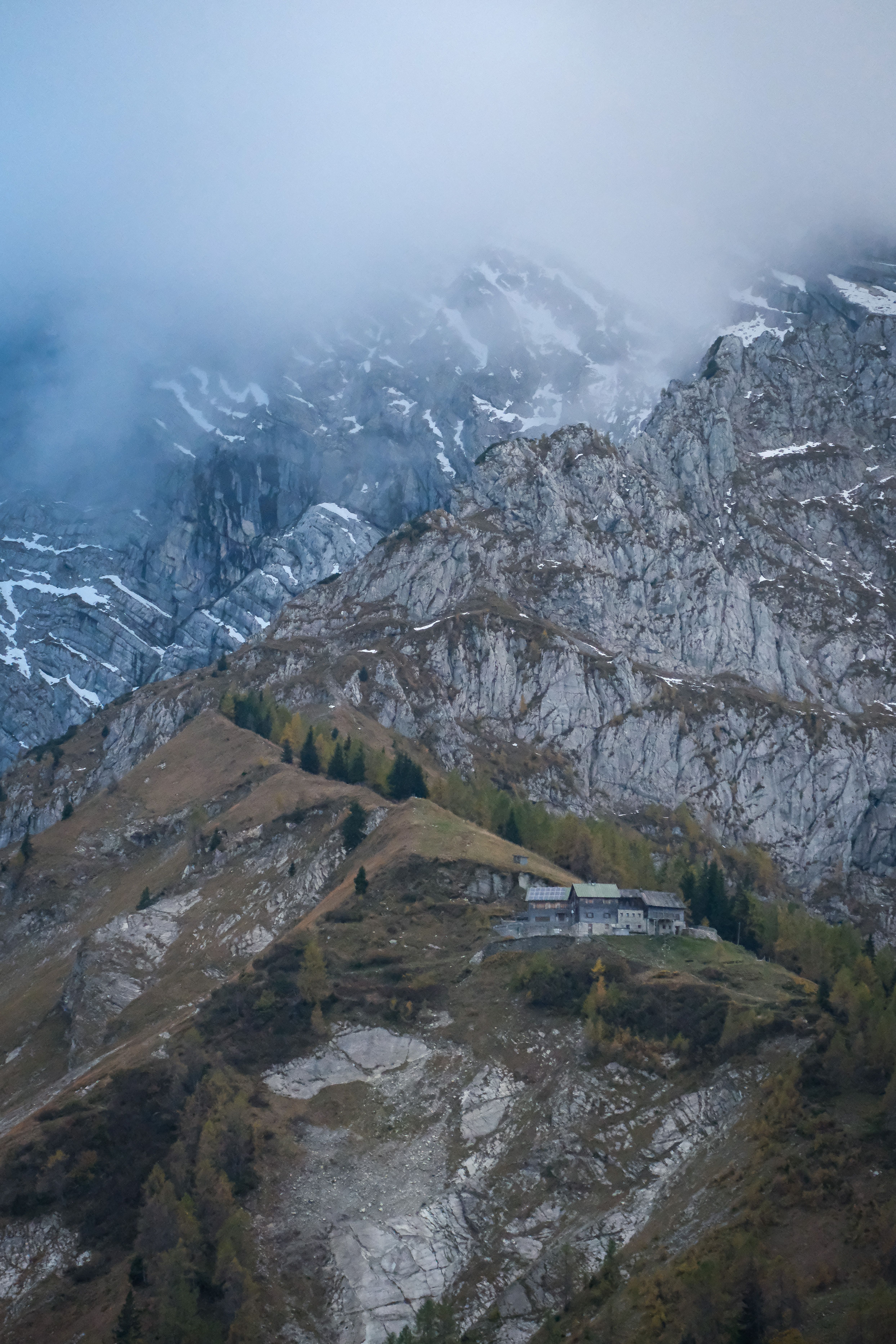 A breathtaking view of a misty mountain range with a remote cabin nestled on a hillside.