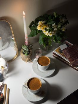 Warm home setting with coffee, candlelight, and florals on a decorative table.